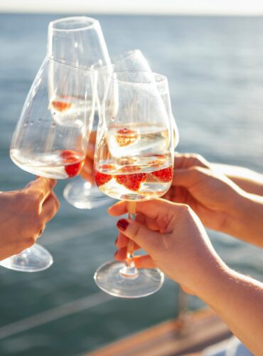 Female,Hands,Holding,Glasses,Of,Champagne,With,Raspberries,On,Board